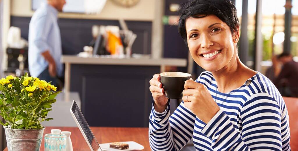 A smiling lady holds a coffee mug looking at the camera.