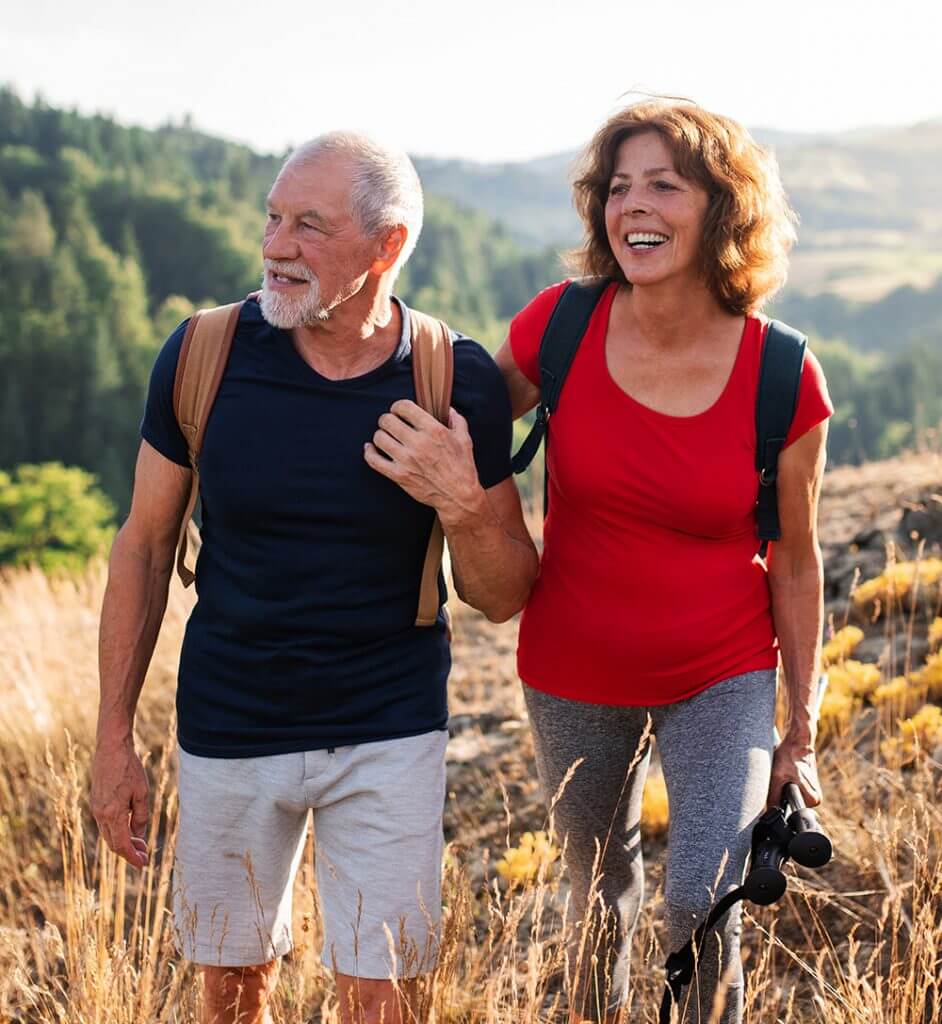 Senior couple carrying backpacks and wearing sports clothes walk a hiking trail in Ontario, California.